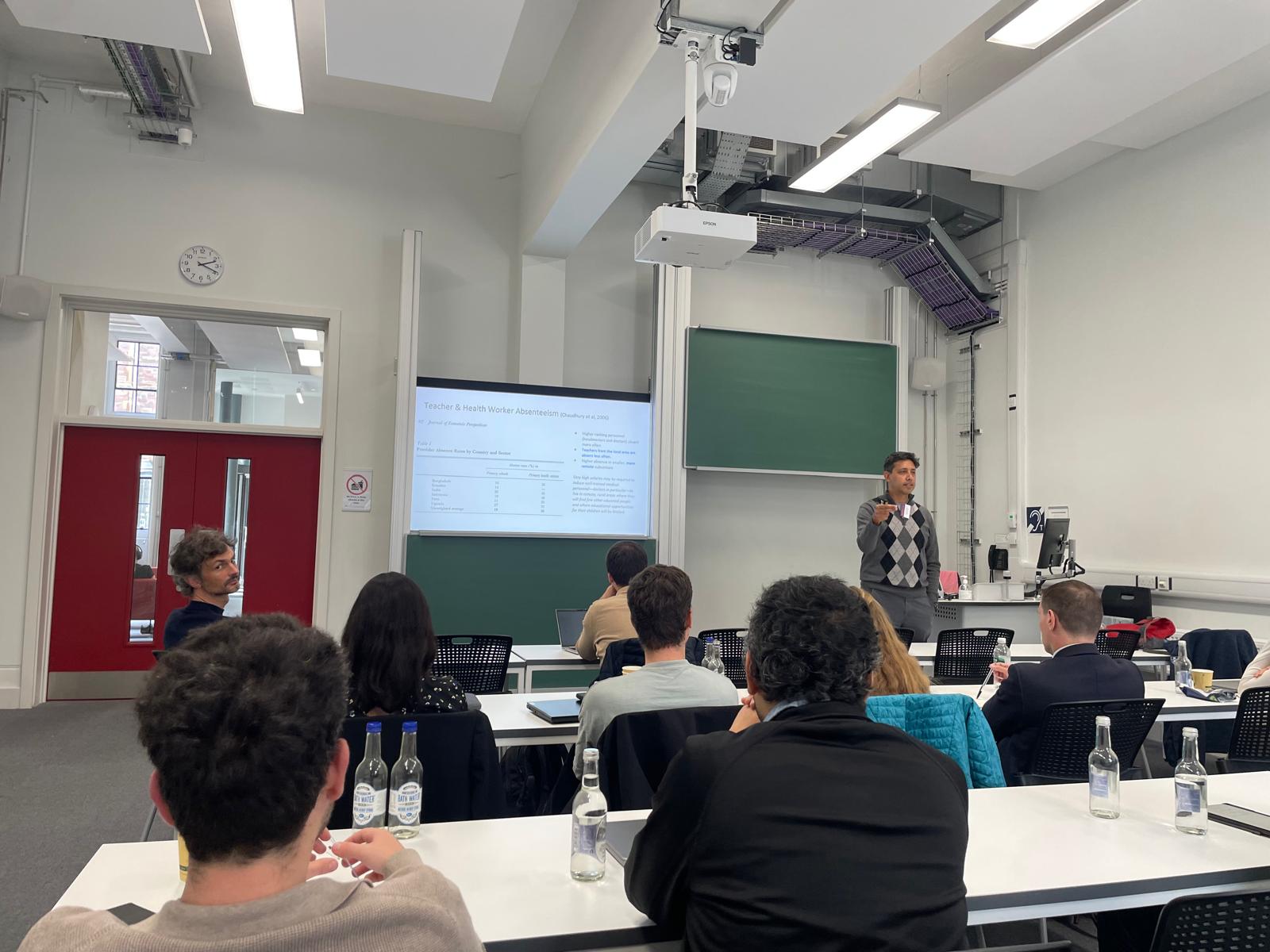 A speaker presenting slides to participants in a lecture room at the BÆM 2026 development economics workshop